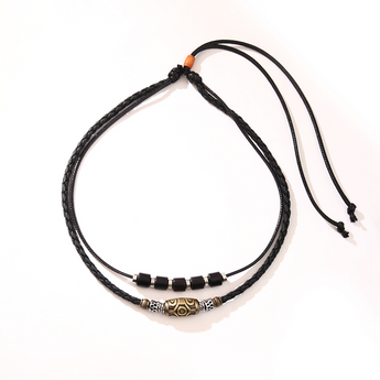 Collar negro de dos cordones con dije de cuentas y nudo ajustable sobre fondo crema