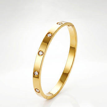 Pulsera rígida delgada dorada con detalles redondos transparentes sobre fondo claro