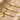 Three gold-tone curved bar bracelets with bow, flower and crown charms, engraving close-up